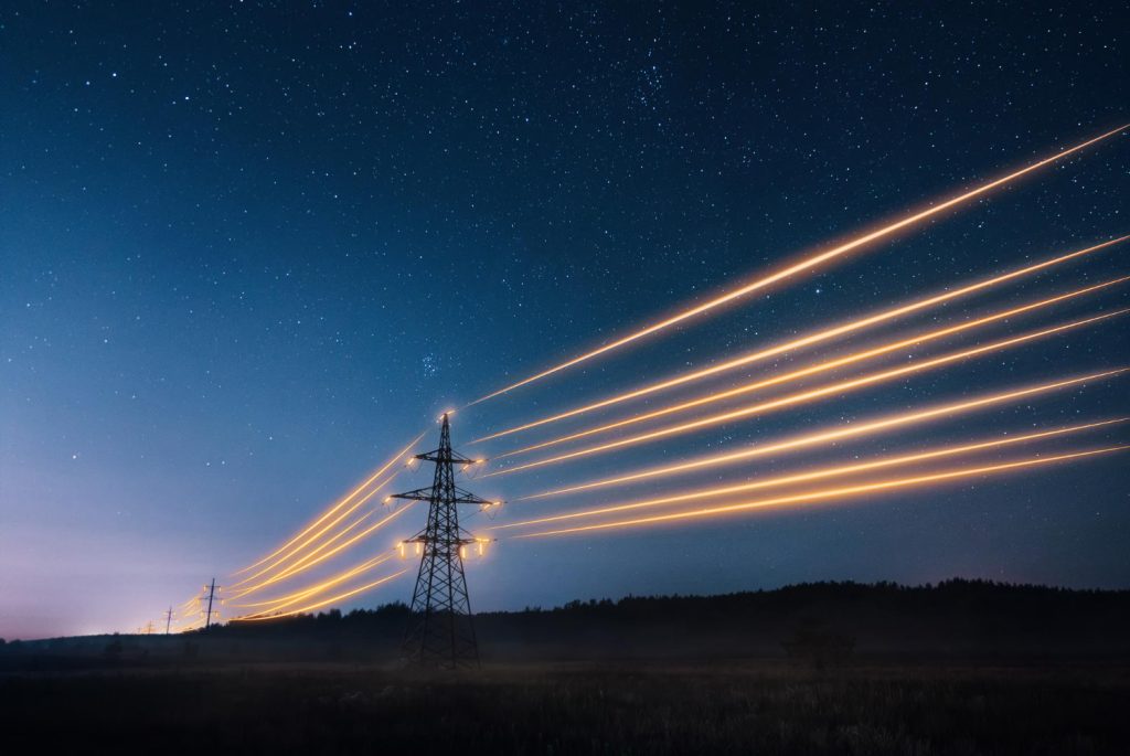 electricity transmission towers with orange glowing wires against night sky