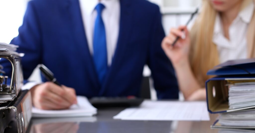 binders with papers are waiting be processed with businessman secretary back blur internal revenue service inspector checking financial document